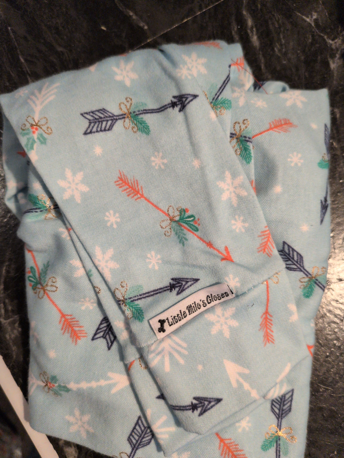 Folded light blue Christmas bodysuit printed with arrows, holly and white snowflakes, with brand label