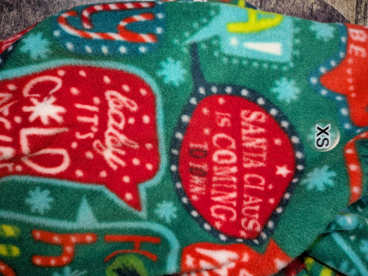 Close-up of green Christmas fleece jammies with red speech bubbles of holiday song words and an XS tag