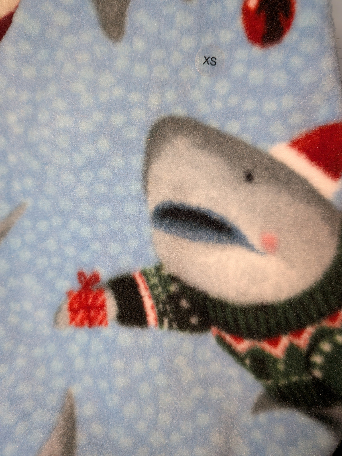 Close-up of light blue Santa Sharks fleece jammies with a shark in a Santa hat and sweater, XS tag