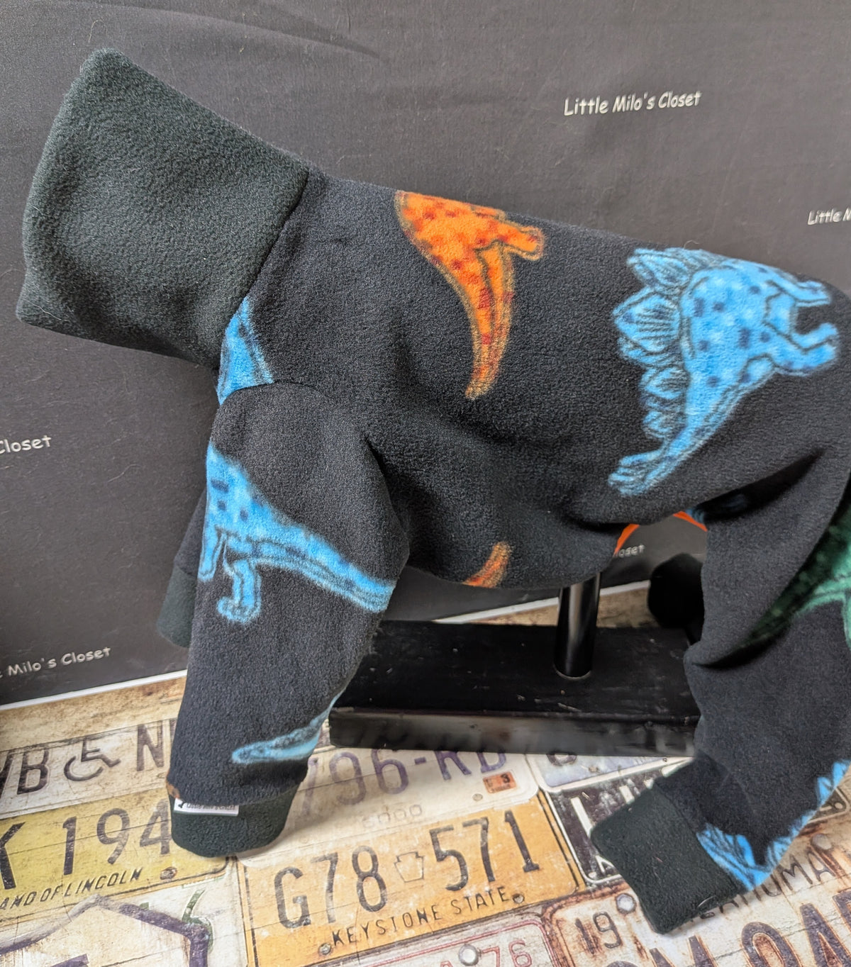 Black fleece bodysuit with bright blue, orange and green dinosaurs, side view on a dog form