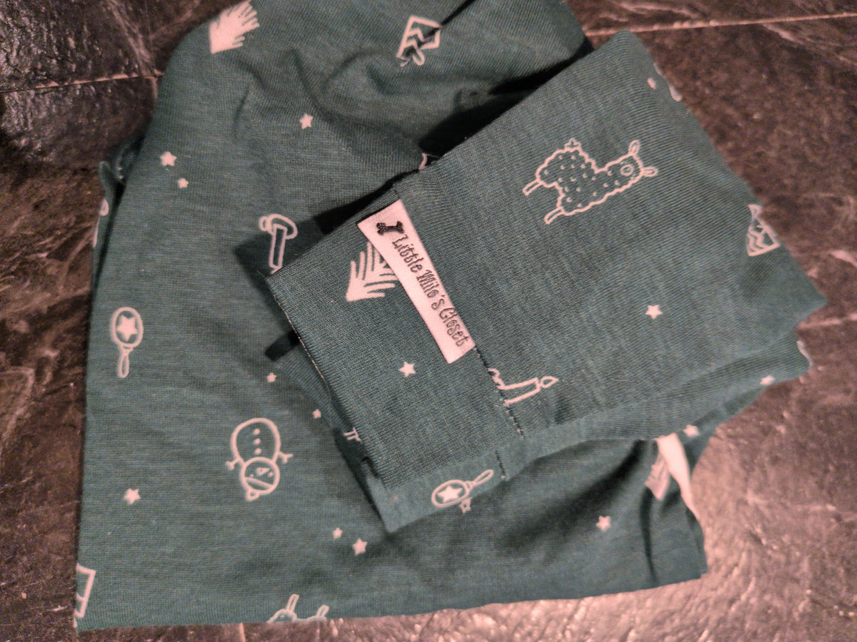 Folded dark teal Christmas bodysuit with pink outline llamas, snowmen and stars, close-up with label