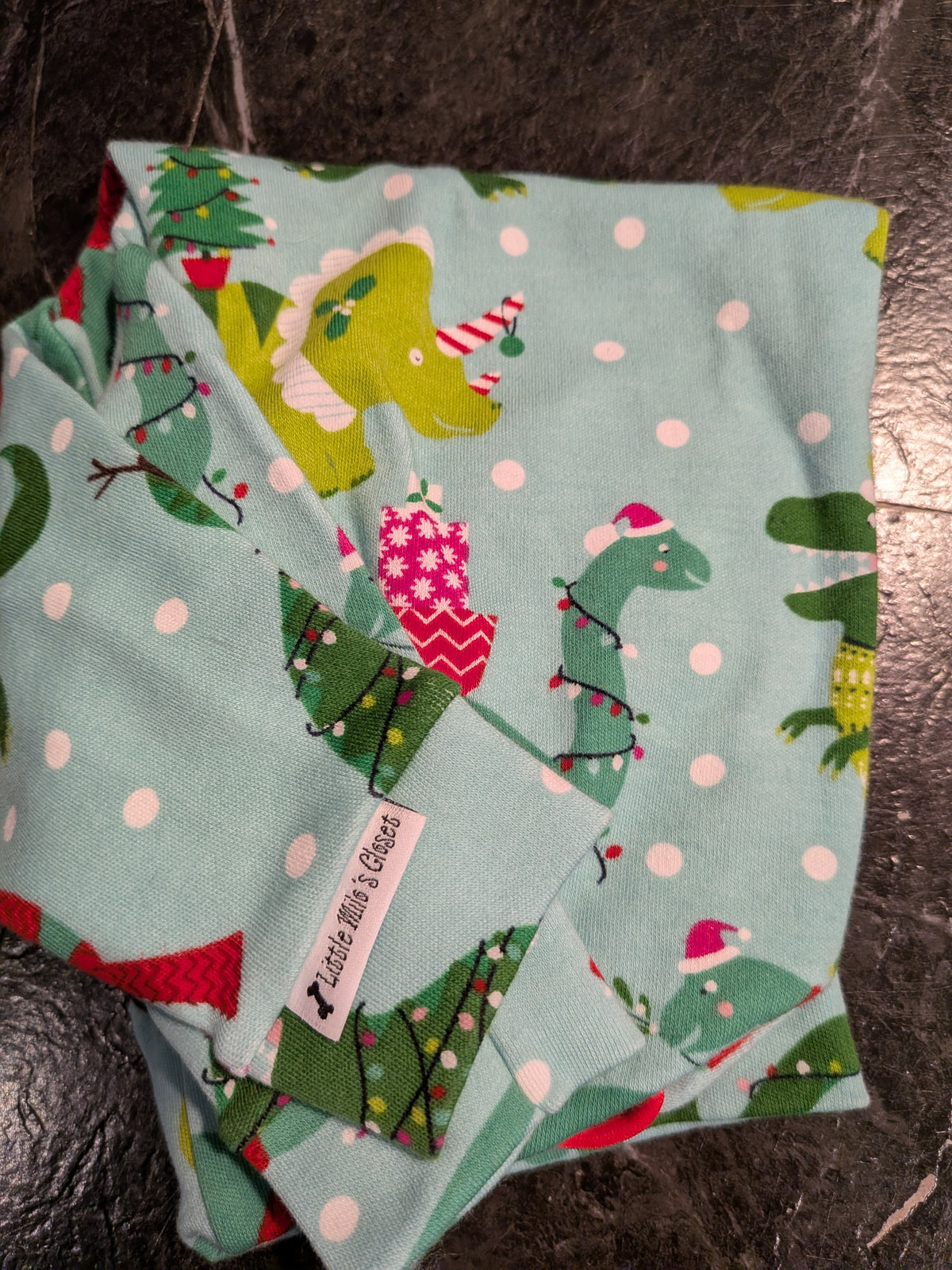 Folded mint polka dot Christmas bodysuit with green dinosaurs in Santa hats wrapped in holiday lights