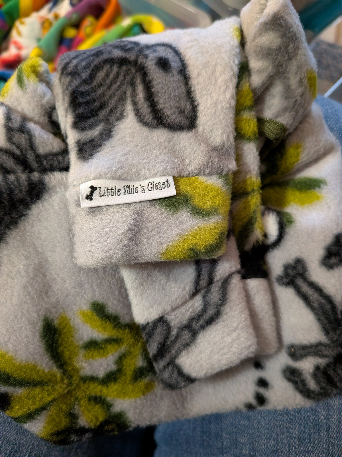 Close-up of a folded light grey plush fleece bodysuit with a grey and lime jungle print and brand label