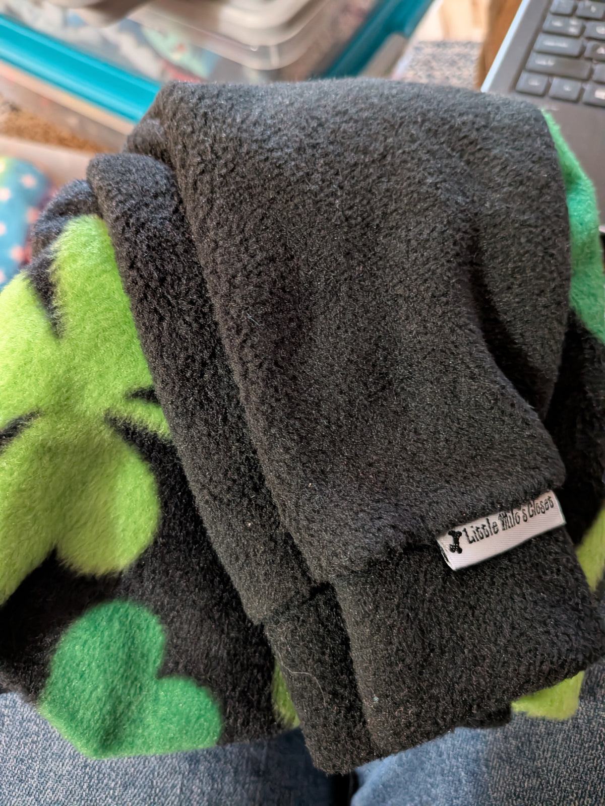Folded black plush fleece bodysuit with lime green shamrock print, solid black sleeves and brand label