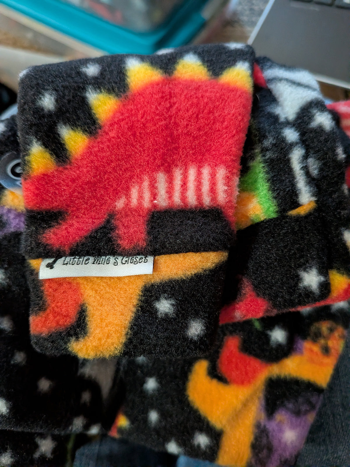 Folded black plush fleece bodysuit with red and orange dinosaurs and white stars, brand label on cuff