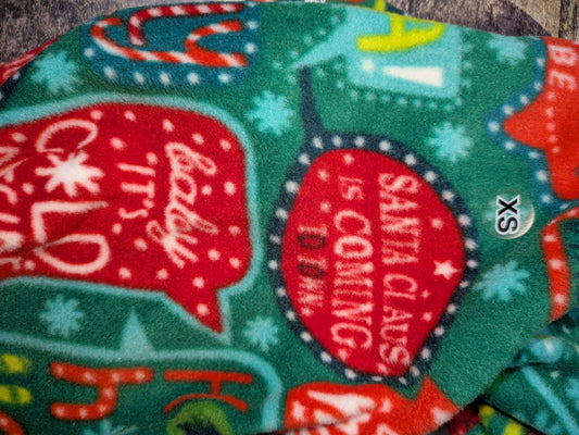 Close-up of green Christmas fleece jammies with red speech bubbles of holiday song words and an XS tag