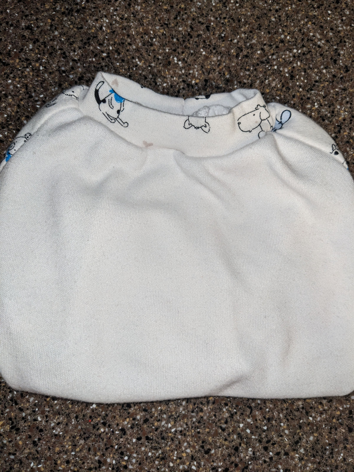 White upcycled dog shirt with a small cartoon dog print around the neckline, folded flat lay