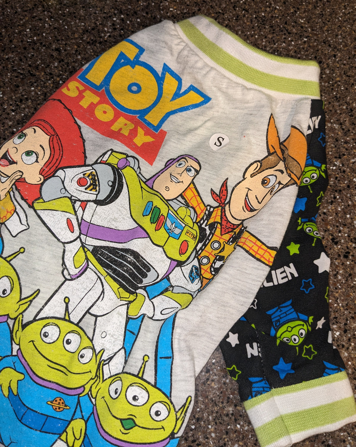 Upcycled Toy Story dog shirt with Buzz, Woody and the little green aliens, flat lay on a speckled counter